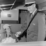 825000 Afbeelding van een conducteur van de N.S. met een nieuw uniform, tijdens het controleren van de kaartjes in een trein.
